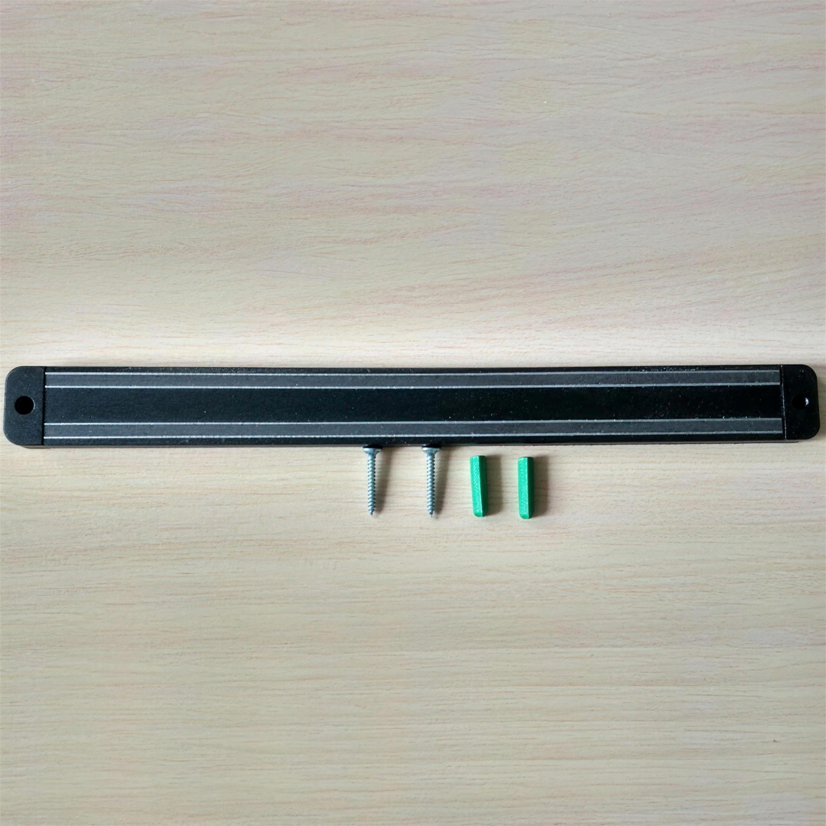 Magnetische Messerleiste 33 cm in Schwarz, daneben zwei Schrauben und zwei Dübel, Aufsicht auf hellem Holz
